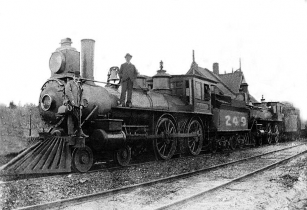 Photographie ancienne d’un homme debout sur la locomotive du train-du-nord en gare de Saint-Jérôme en 1876.