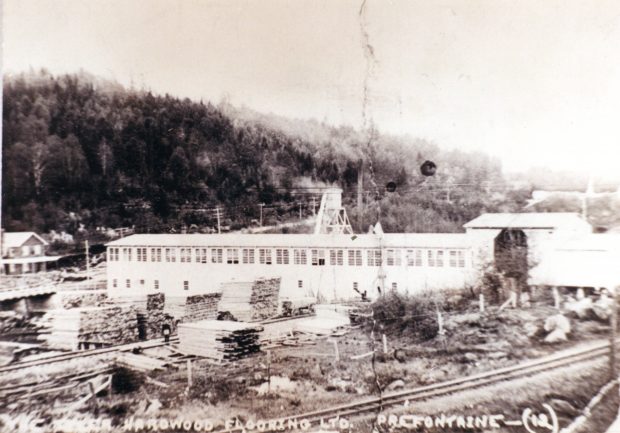 Photographie ancienne montrant les piles de planches de bois auprès des voies ferrées et des moulins à bois de la Tyler Hardwood Flooring à Préfontaine en 1923.