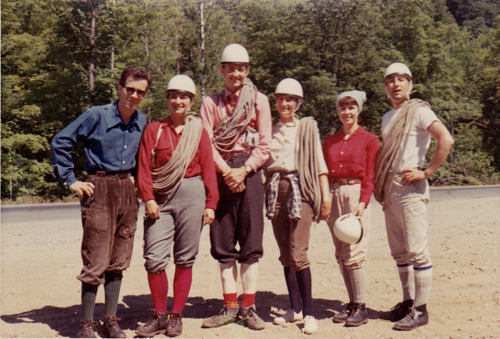 Un groupe de six grimpeurs et grimpeuses, sur un chemin devant une forêt, avec leurs casques et des cordes.