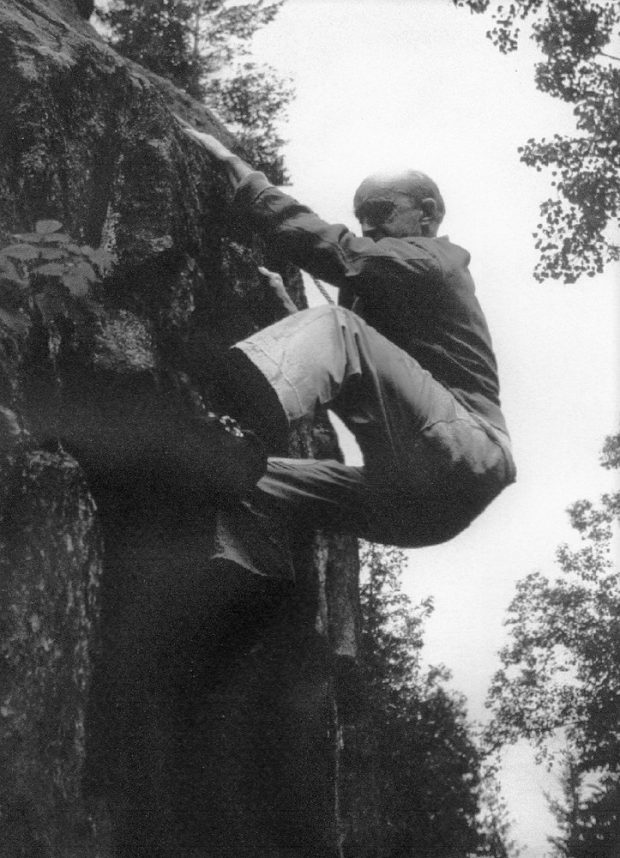 Grimpeur sur une paroi rocheuse de Val-David. Rattaché par une corde, il ne semble pas porter d’équipement particulier.