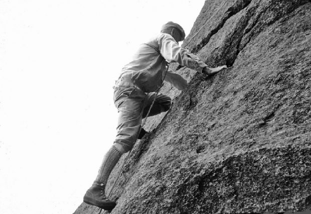 John Brett grimpant une paroi inclinée en montagne.