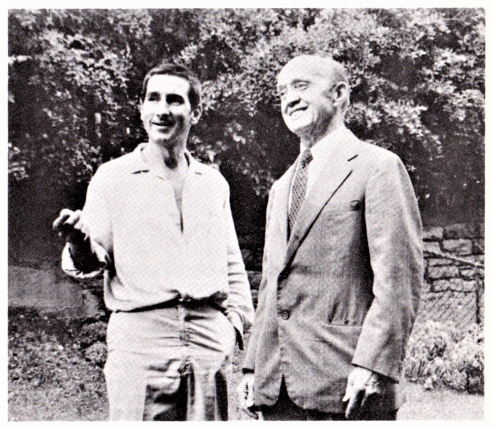 Photographie ancienne de deux hommes qui discutent; le protagoniste de gauche montre de la main quelque chose devant lui.