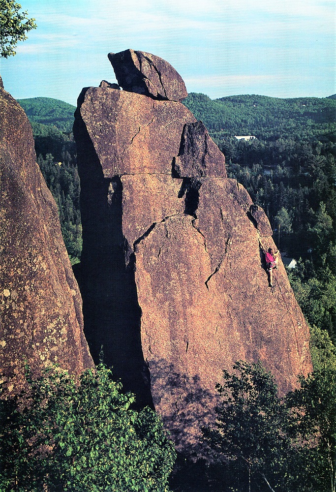 Vue d’une jeune femme accrochée par ses pieds et ses mains sur l’Aiguille du mont Condor, une immense pièce de rocher brun-orangée d’environ 23 mètres de hauteur.