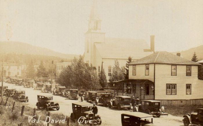 Vue du village avec rue principale, église et vieilles voitures