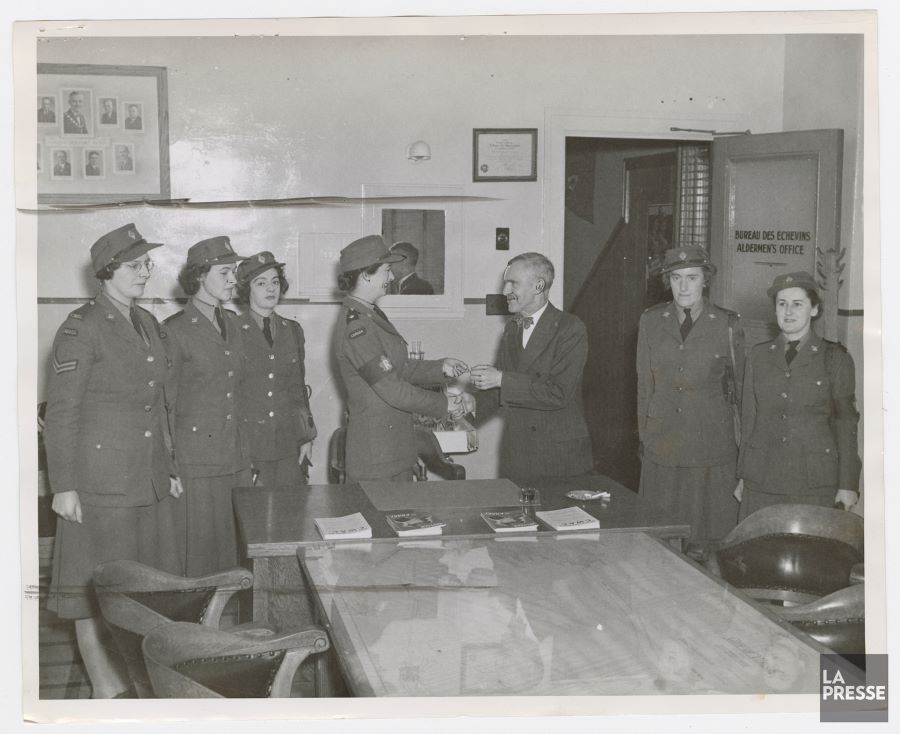 Photographie en noir et blanc d'une petite salle avec la porte ouverte.. Au centre, le maire Wilson remet les clés à l'une des six femmes en uniforme. Ces sept personnes sont debout autour d'une table.