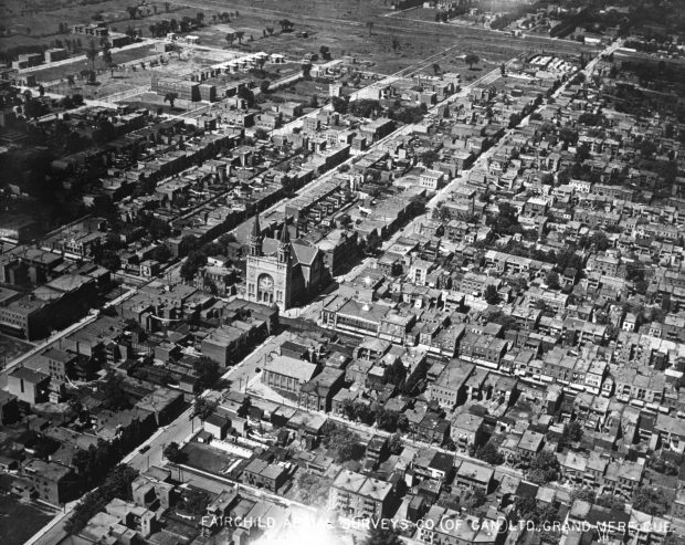 Photographie aérienne oblique en noir et blanc des rues et des bâtiments du secteur le plus urbanisé de Verdun. Les rues sont rectilignes et se croisent à angle droit.