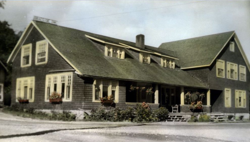 Une carte postale colorisée montre une auberge avec un balcon couvert et des jardinières aux fenêtres.