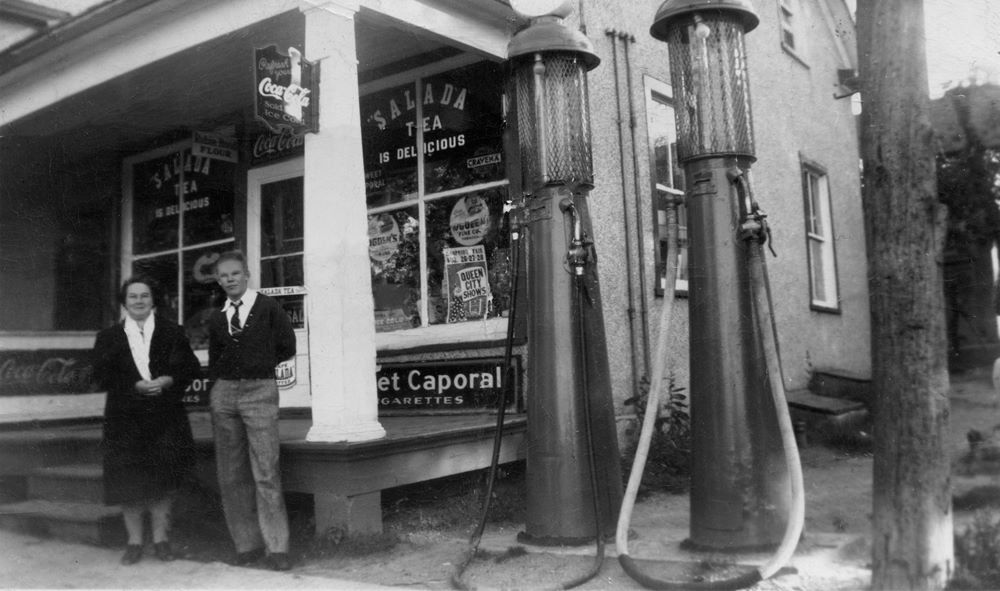 Un homme et une femme se tiennent debout à côté de pompes à essence anciennes devant un magasin général.