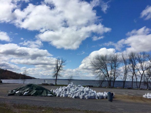 Deux tas de sacs de sable déposés dans un stationnement près de la rivière.