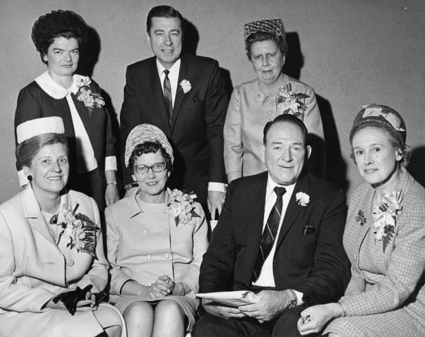 Photo en noir et blanc de cinq femmes et deux hommes. Le groupe est élégamment vêtu, y compris avec des bouquets de corsage.
