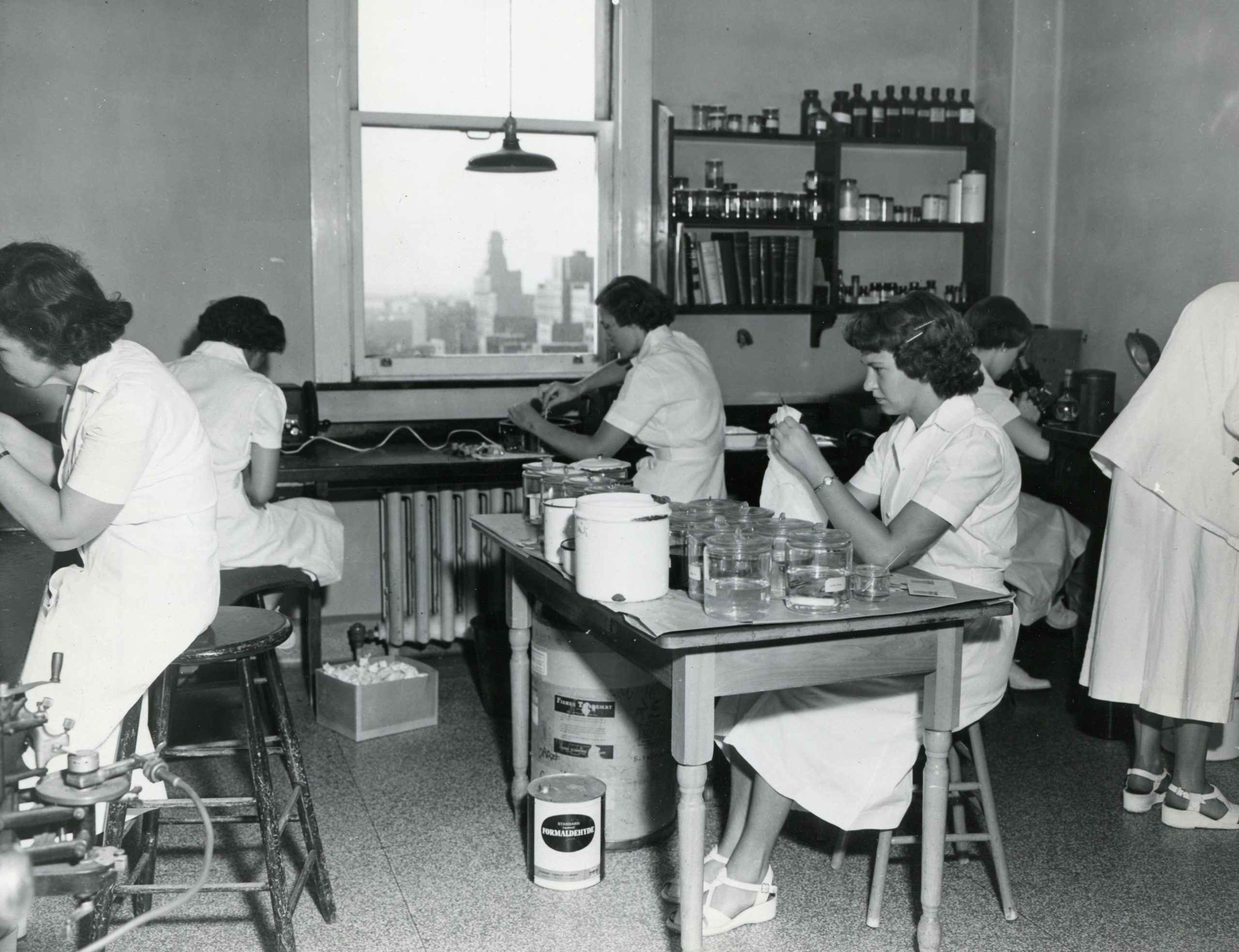 Photo en noir et blanc de jeunes femmes en sarrau de laboratoire accomplissant diverses tâches dans le laboratoire.