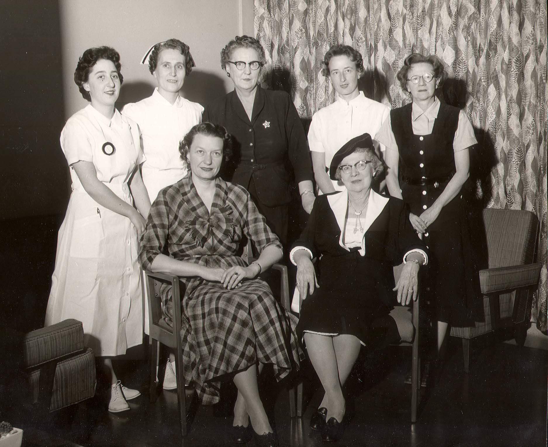 Photo en noir et blanc de sept femmes. Deux d’entre elles sont assises, et plusieurs de celles debout portent un uniforme d’infirmière.