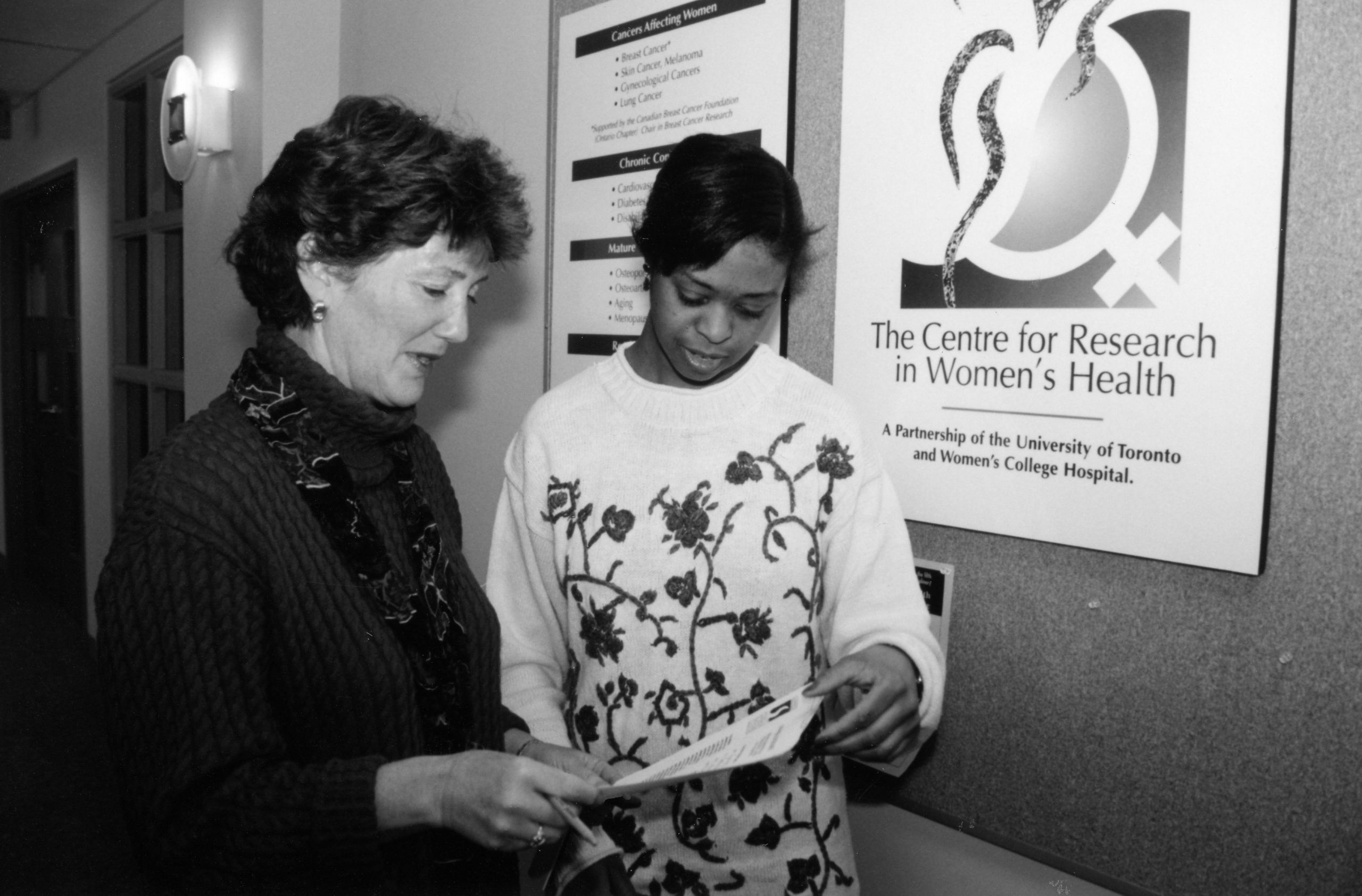 Deux femmes examinent une brochure; une grande enseigne sur le mur à côté annonce le « Centre for Research in Women's Health ».