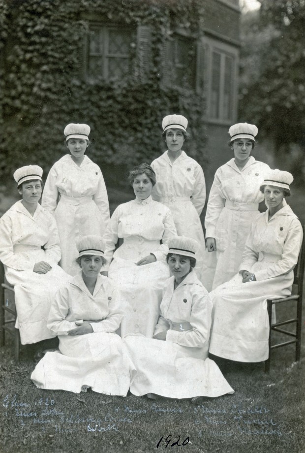 Huit femmes en uniforme d’infirmière complet debout, assises ou à genoux, souriant pour l’appareil photo.