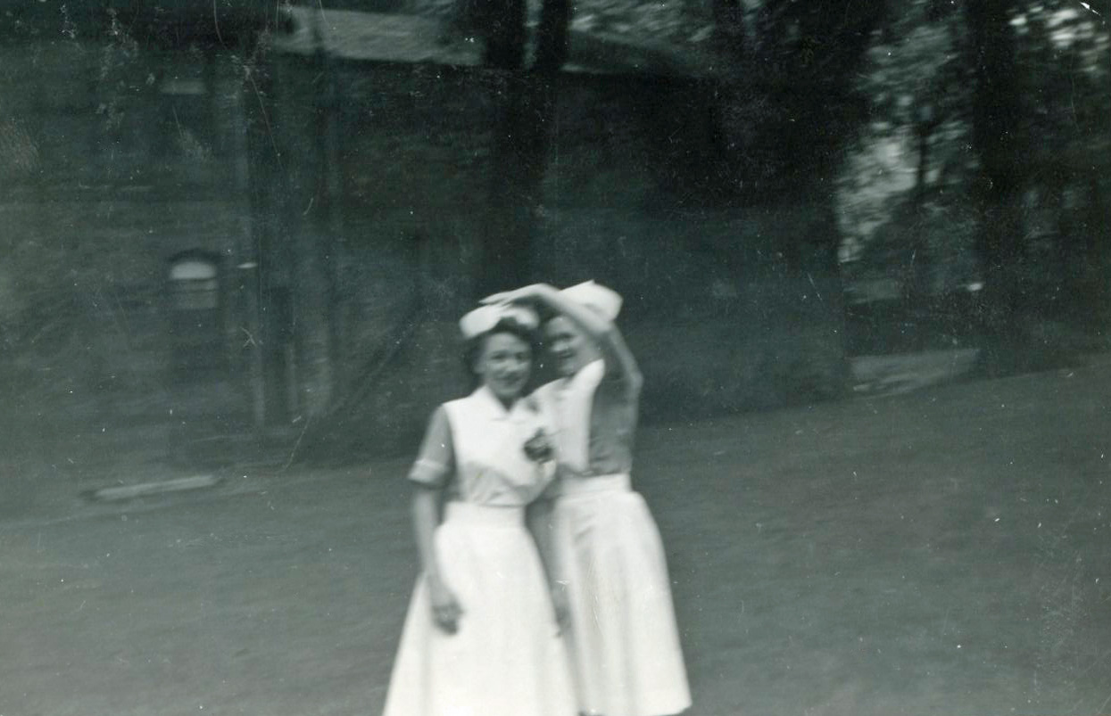 Deux femmes souriantes dehors, en uniforme d’infirmière.