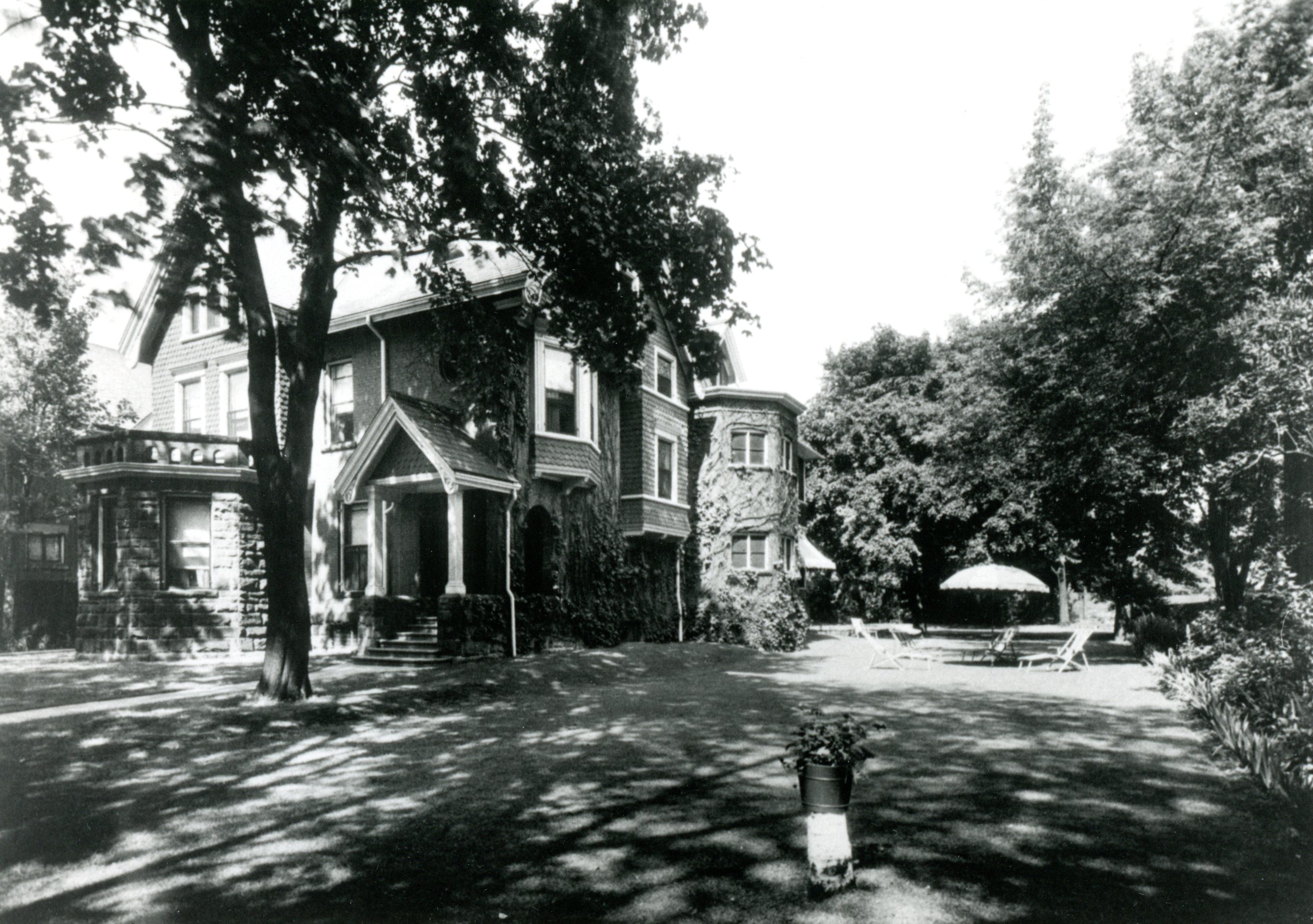 Maison couverte de vignes et entourée d’arbres, avec pelouse généreuse.