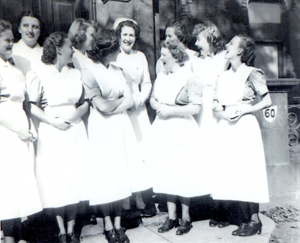 Dix jeunes femmes en uniforme rient. L’une d’entre elles porte une coiffe d’infirmière.