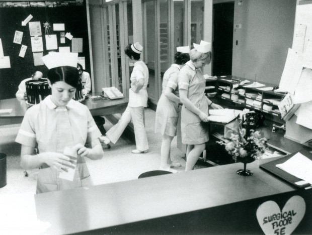 Six personnes parlent et manipulent des documents dans une aire de réception. Quatre femmes portent une cape d’infirmière.