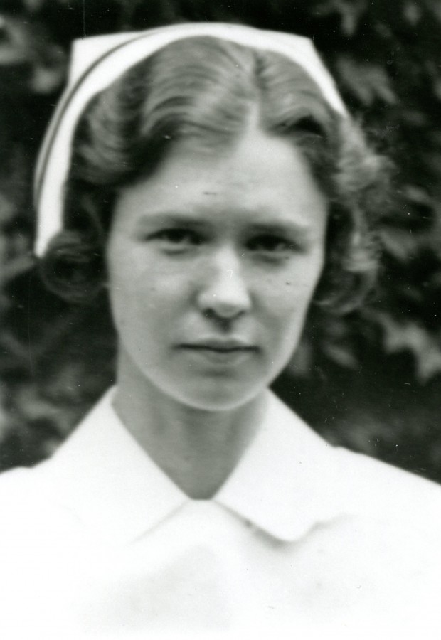 Une jeune femme portant une coiffe d’infirmière avec bande noire pose pour une photo.