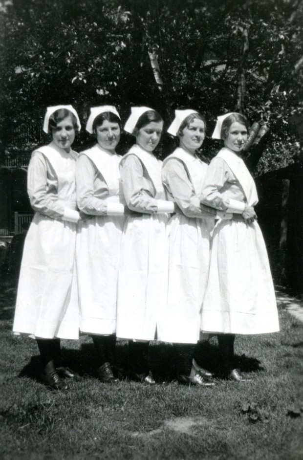 Cinq jeunes femmes posent dehors pour une photo officielle. Elles portent des uniformes et coiffes d’infirmière.
