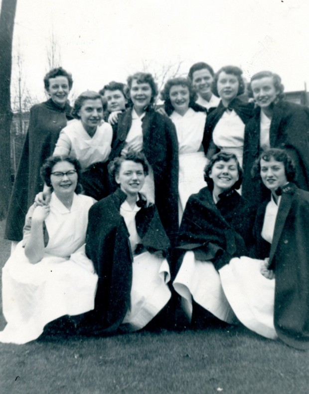 Douze jeunes femmes sourient et posent pour l’appareil photo. Elles sont dehors, et la plupart portent une cape d’infirmière par-dessus leur uniforme.
