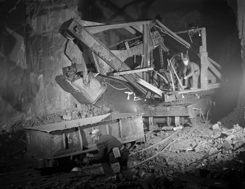 Une pelle mécanique chargeant du minerai de fer dans un wagon et deux ouvriers dans un puits de mine