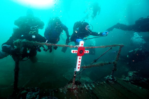 Un groupe de plongeurs sur une épave, près d’une croix couverte de coquelicots.