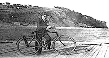 un adolescent en costume se tient debout, avec sa bicyclette, sur un quai