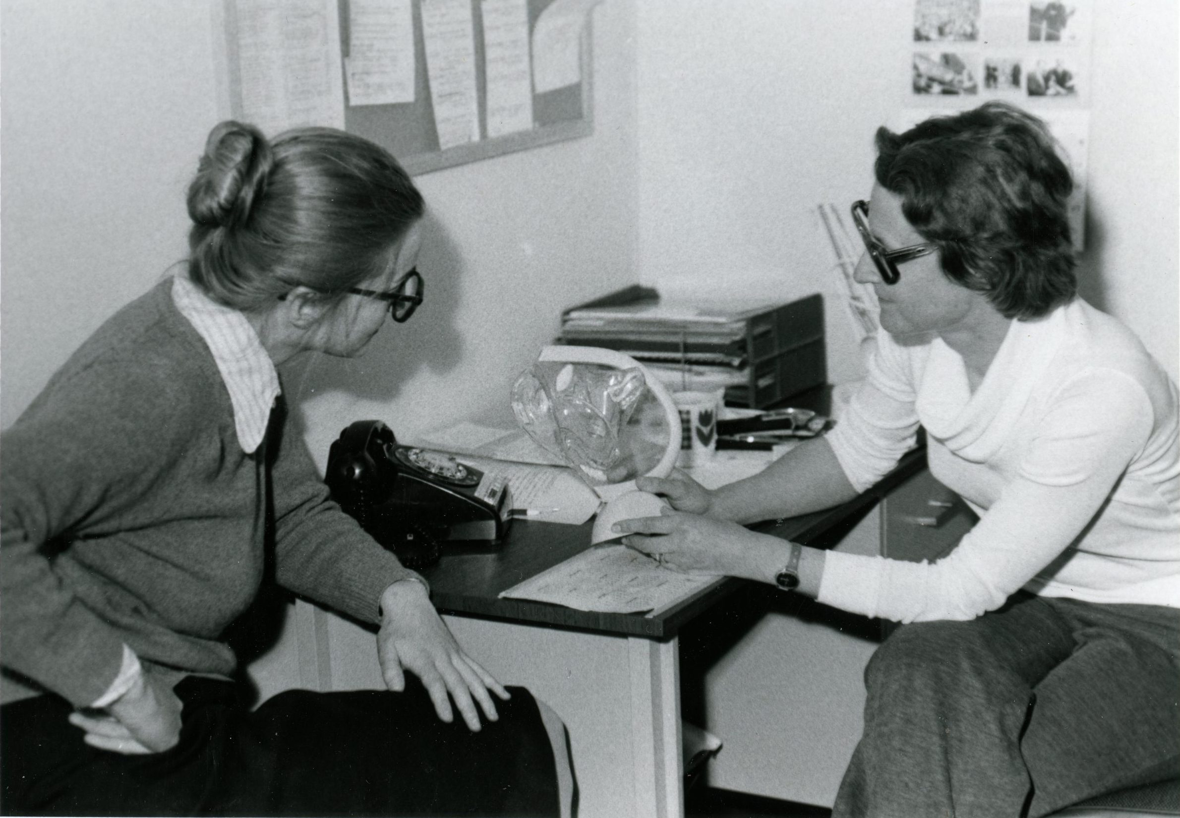 Discussion entre deux femmes assises à une table de travail dans un bureau. Une femme tient un modèle médical transparent.