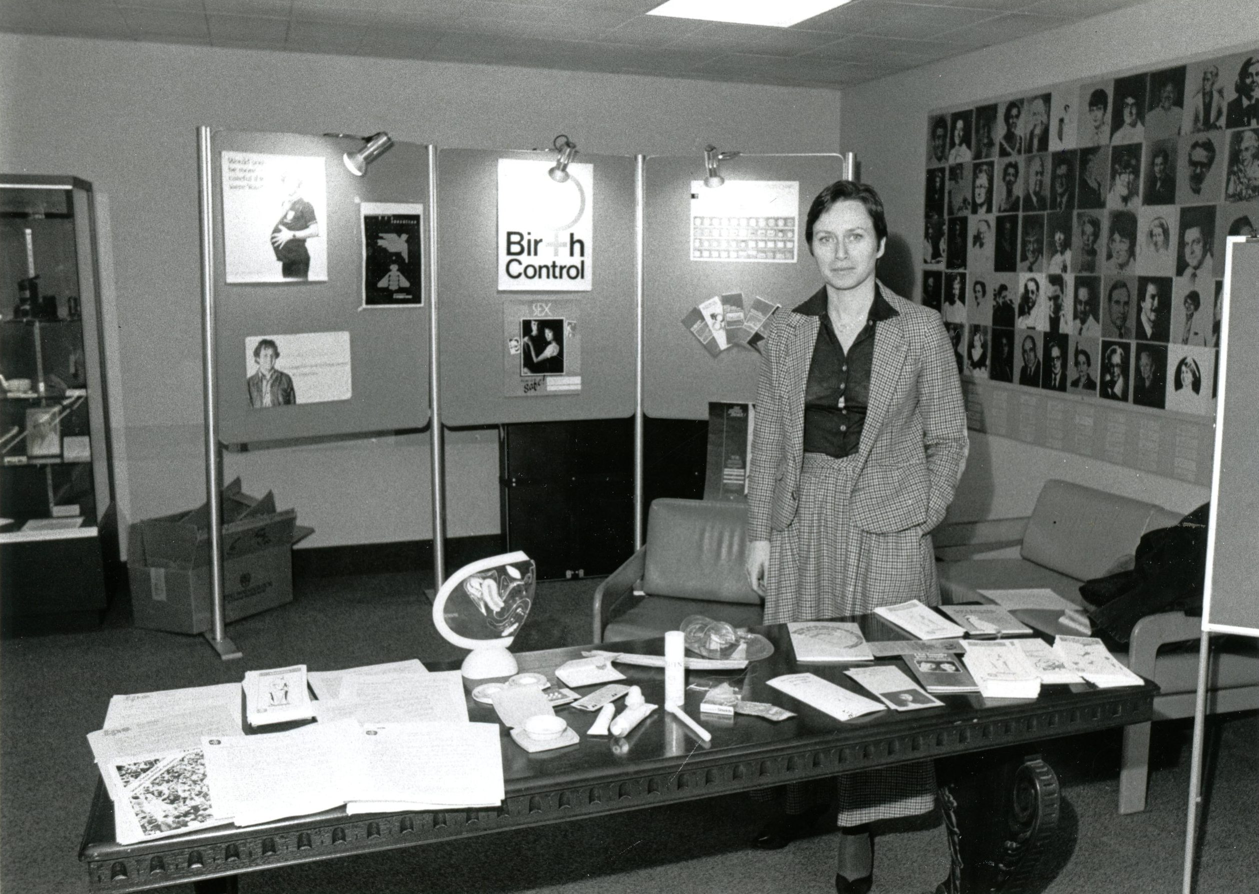 Une femme debout derrière une table couverte de diverses ressources éducatives se rapportant à la contraception. 