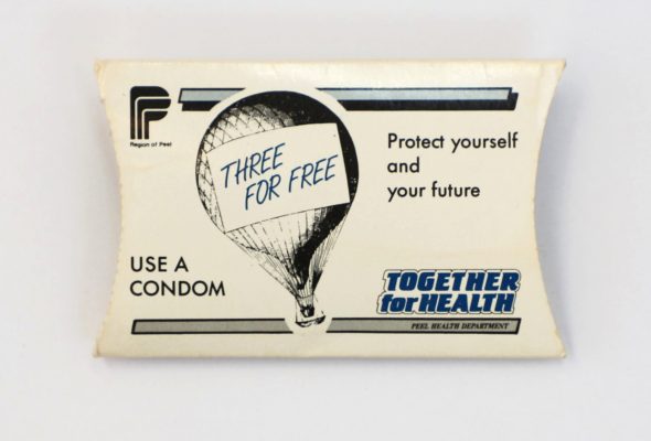 A small, rectangular, cream-colored condom packet with black and blue text and graphics on it. It features a black and white illustration of a hot air balloon with the phrase THREE FOR FREE written on it.