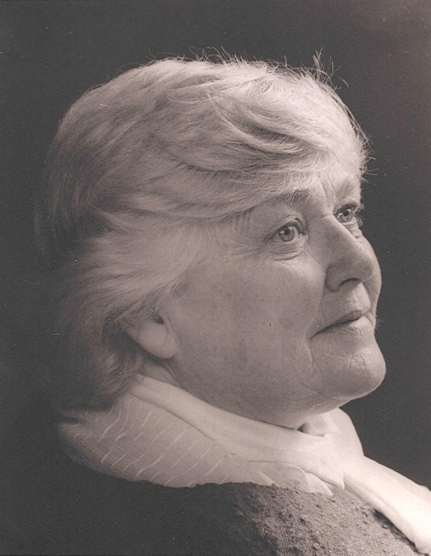 Portrait en noir et blanc d’une femme d’âge mûr aux cheveux courts et ondulés portant une écharpe de couleur pâle; elle est de profil et regarde vers la droite.