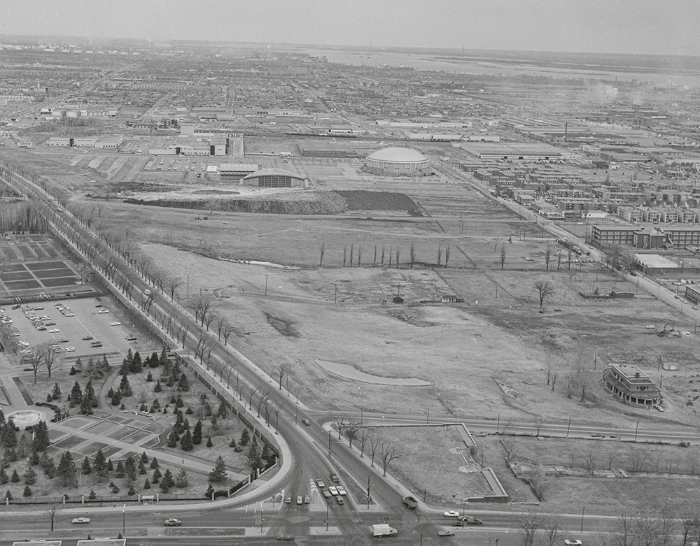 En noir et blanc, vue du ciel, le vaste site du Stade olympique, avant sa construction, s’étend à proximité de l’aréna Maurice-Richard, au toit arrondi.
