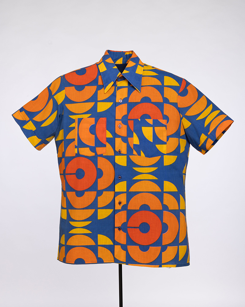 La chemise des techniciens de l’Organisme de radiotélévision des Olympiques affiche le logo de Radio-Canada : sur fond bleu marine, la lettre C, en rouge, se diffuse dans toutes les directions, en orange et jaune.