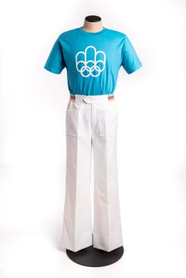 Un mannequin de couture présente l’uniforme des messagers de la presse. Il se compose d’un pantalon blanc évasé à plis, à la taille décorée d’un liseré arc-en-ciel, et d’un t-shirt bleu azur. Le logo blanc des Jeux de 1976 y figure.