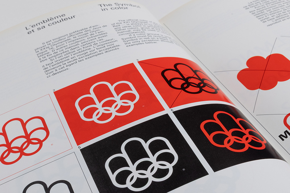 Le manuel de graphisme des Jeux de 1976 est ouvert à la page intitulée L’emblème et sa couleur. En-dessous d’un court texte écrit en français et en anglais, 6 exemples du logo des Jeux olympiques apparaissent sur différents fonds, dans une palette de couleurs réunissant le rouge, le blanc et le noir.