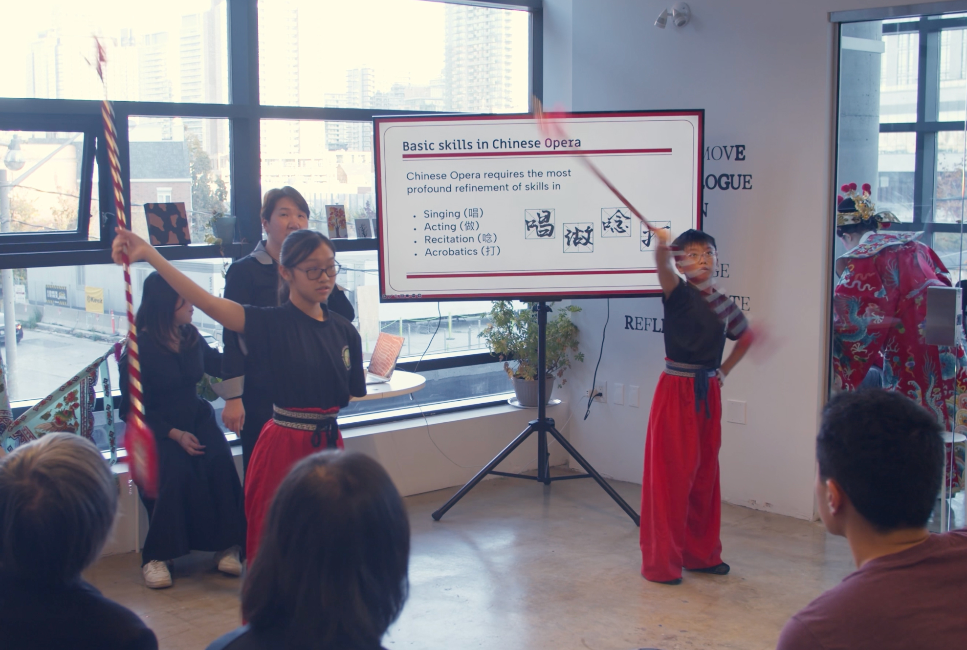 <span style="font-weight: 400;">Two young students stand in front of a PowerPoint presentation, posing with their spears.</span>