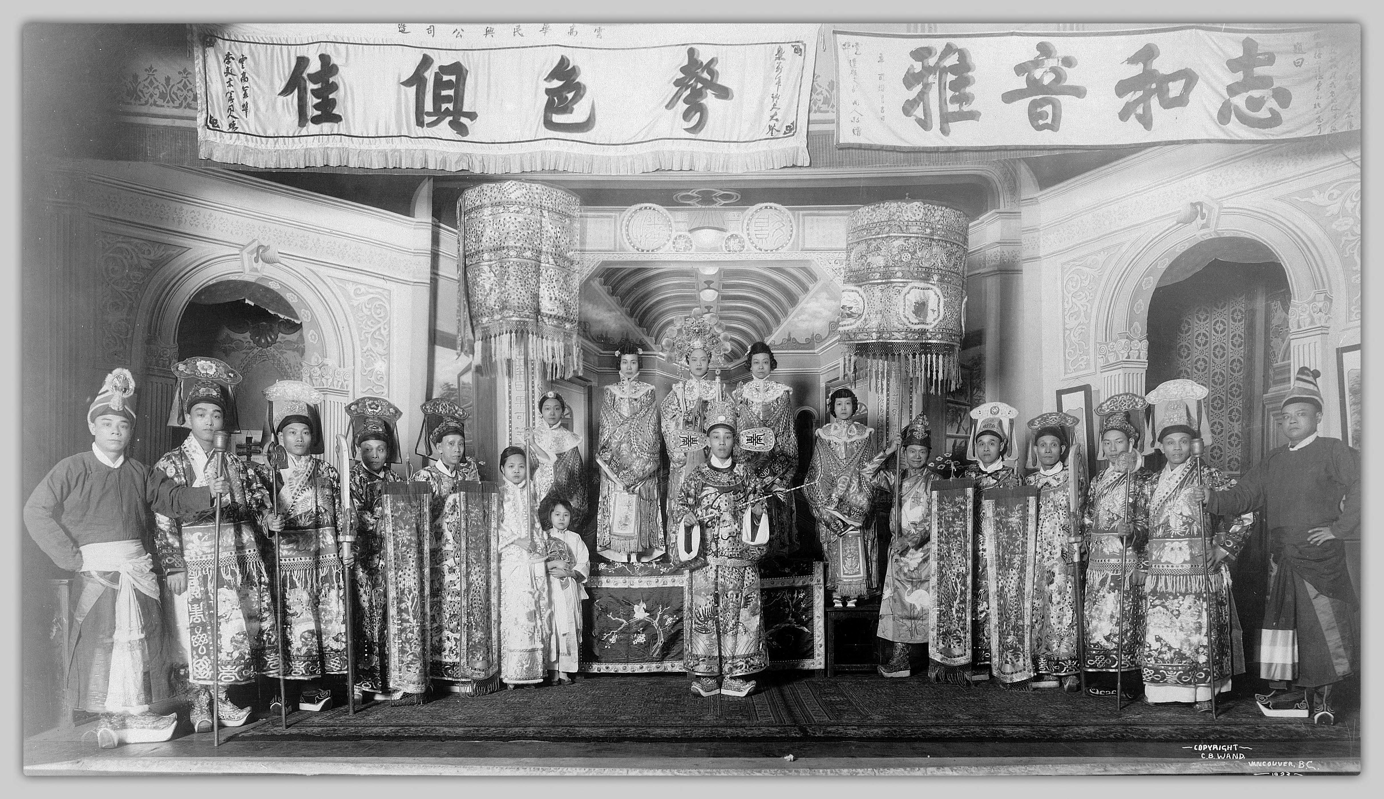 <span style="font-weight: 400;">Dix-neuf artistes en costume sont debout en rang sur scène pour une photo de groupe. Deux longues banderoles horizontales portant des inscriptions en chinois sont suspendues au-dessus du groupe, rendant hommage à la beauté et à l’élégance de leur performance.</span>