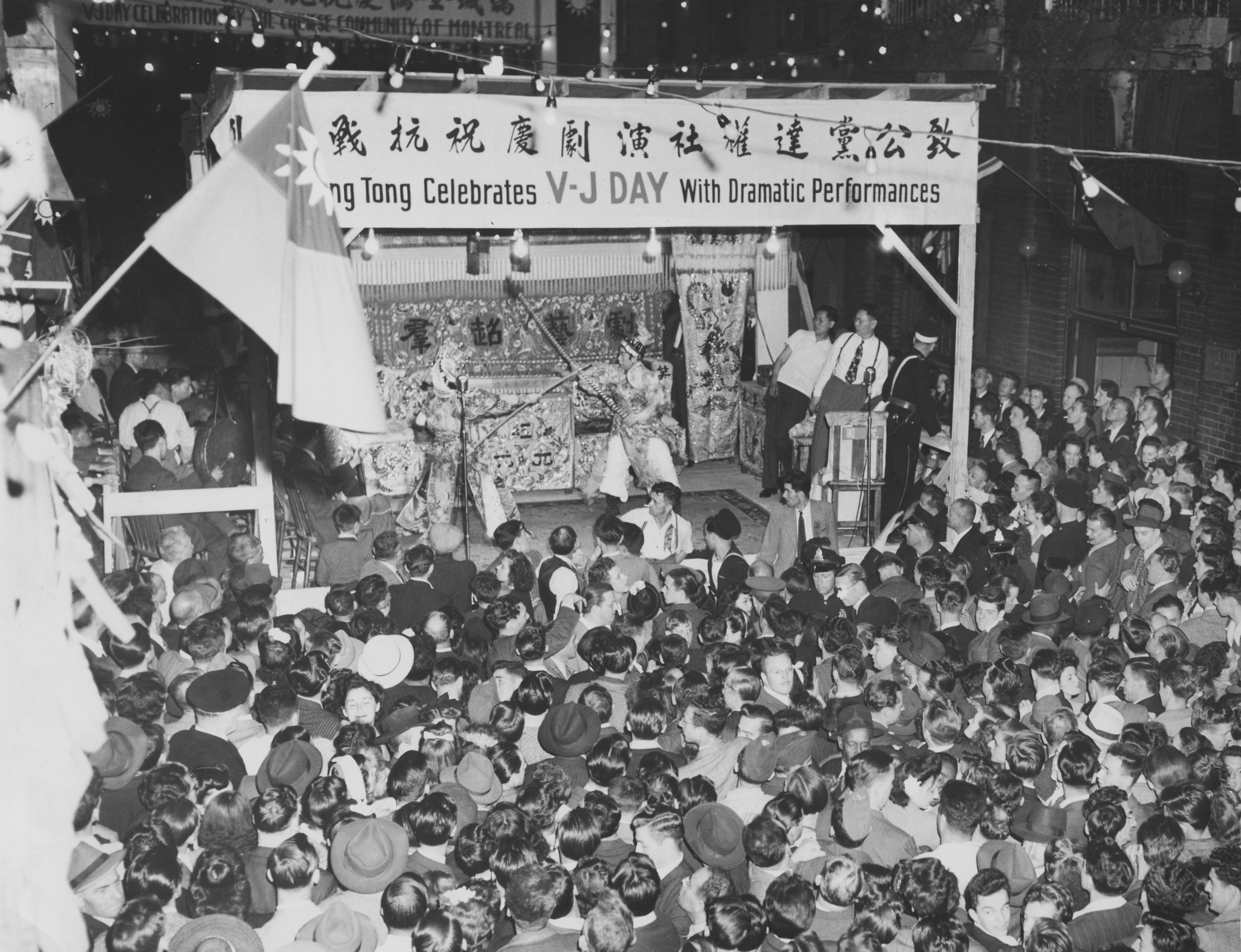 <span style="font-weight: 400;">Une foule nombreuse se rassemble autour d’une scène extérieure dans le quartier chinois. Face à face sur scène, deux artistes se livrent à un combat à la lance.</span>