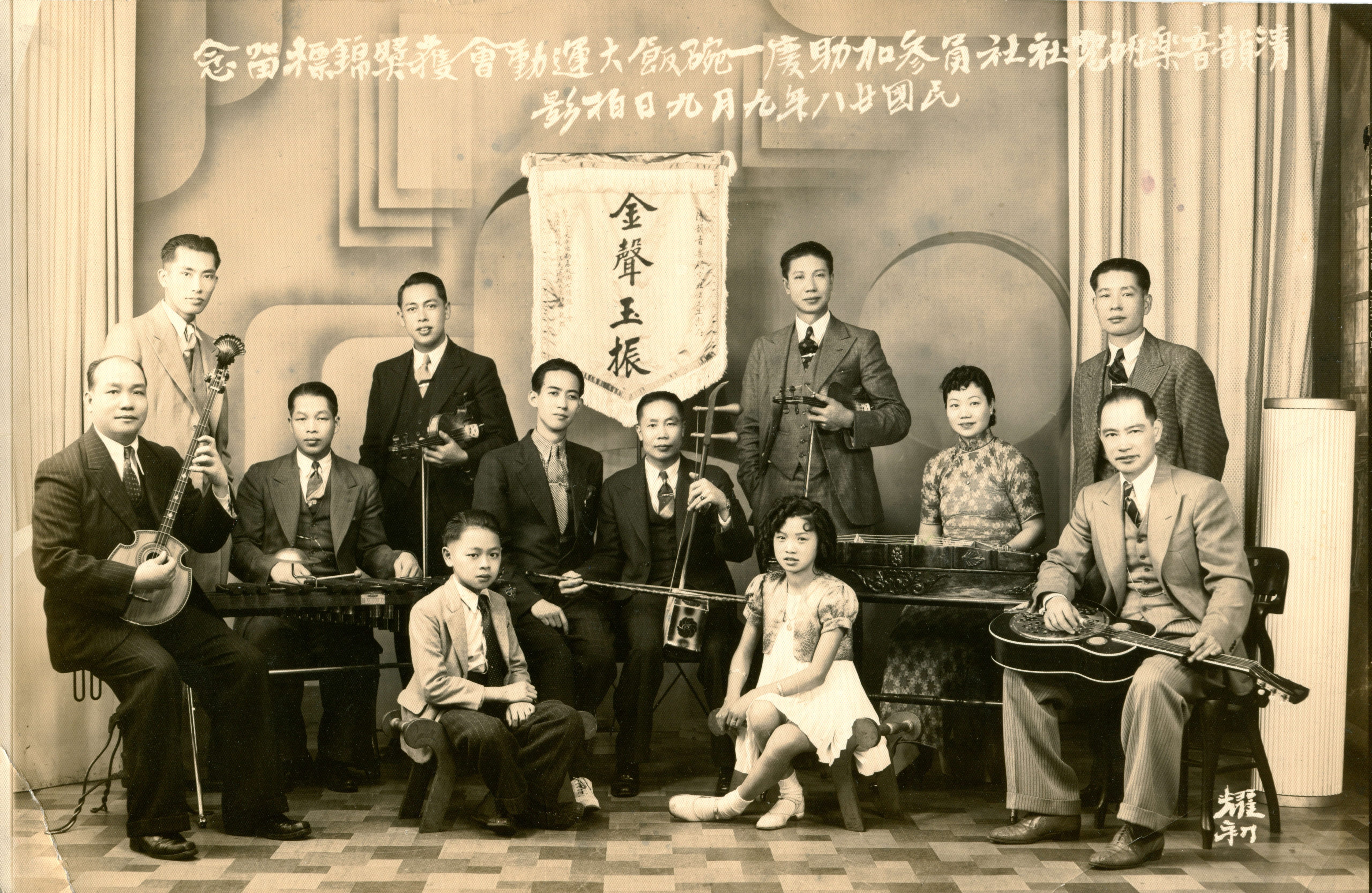 <span style="font-weight: 400;">清韻音樂社成員帶著他們的樂器坐在一幅橫額前。</span>