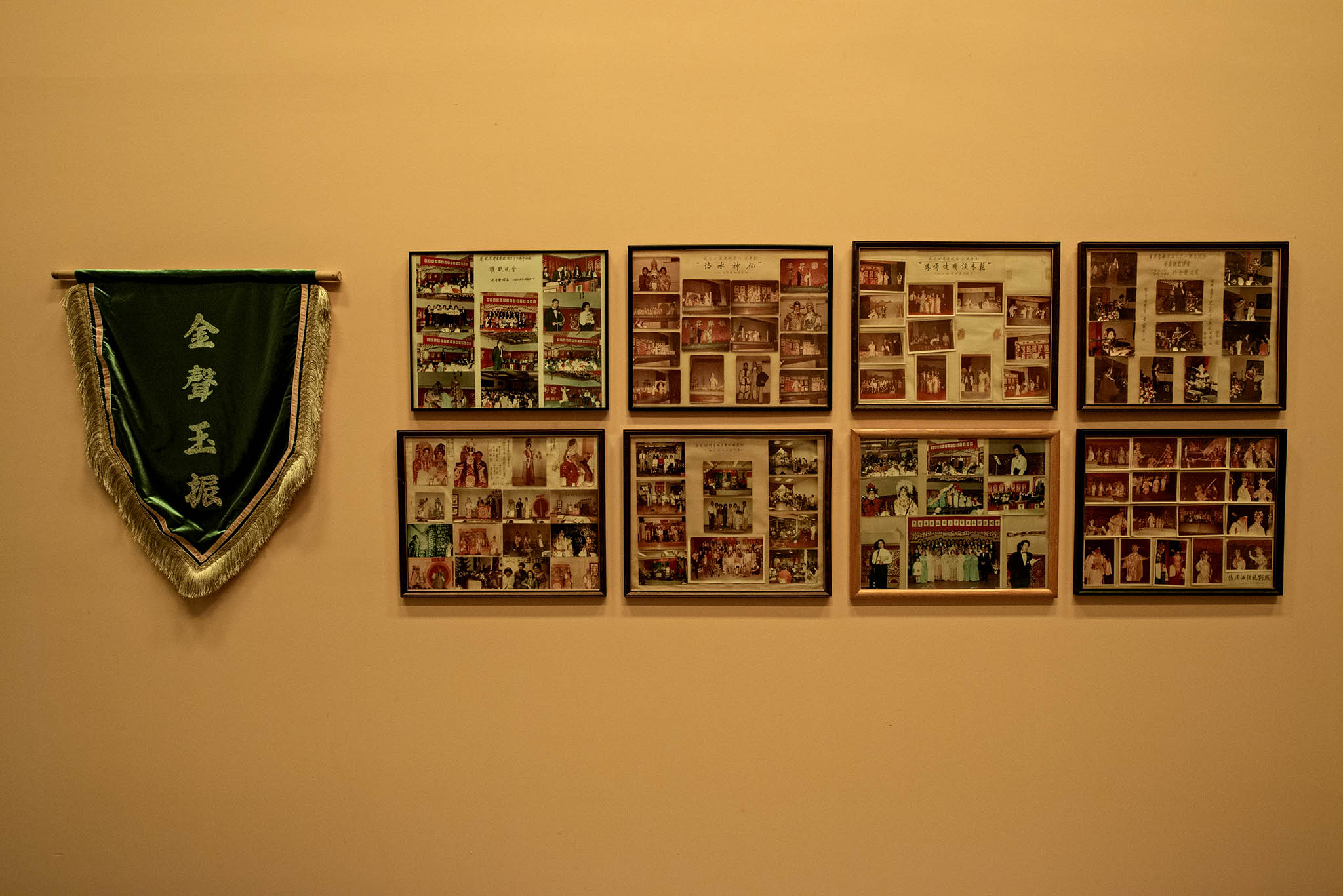 Un assortiment de huit cadres avec de vieilles photos et une banderole suspendue sont disposés sur un mur blanc le long de l’aile latérale de la scène de Parfum des foudres.