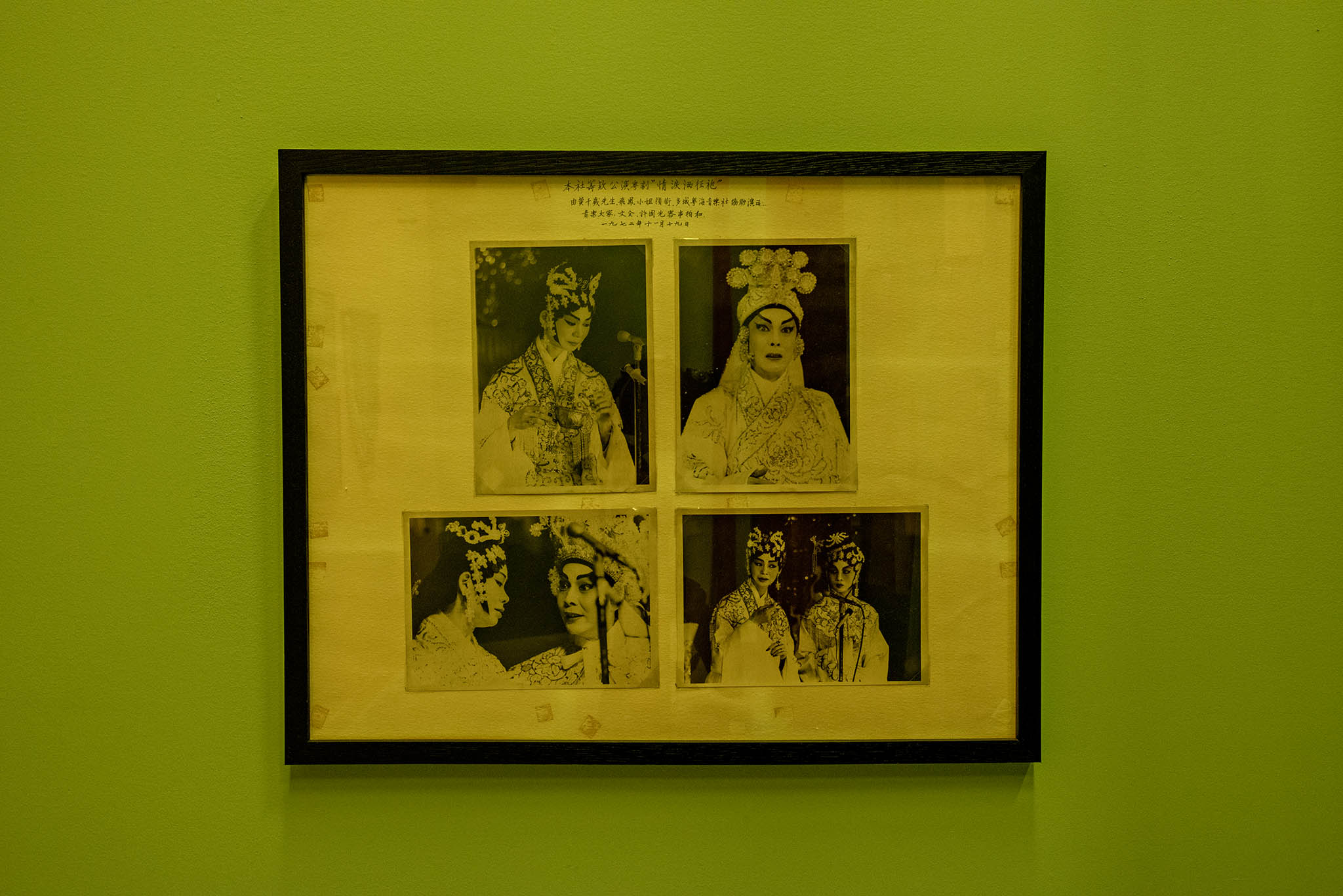 Quatre photos en noir et blanc d’artistes d’opéra cantonais, présentées dans un cadre noir sur un mur vert derrière la scène de Parfum des foudres.