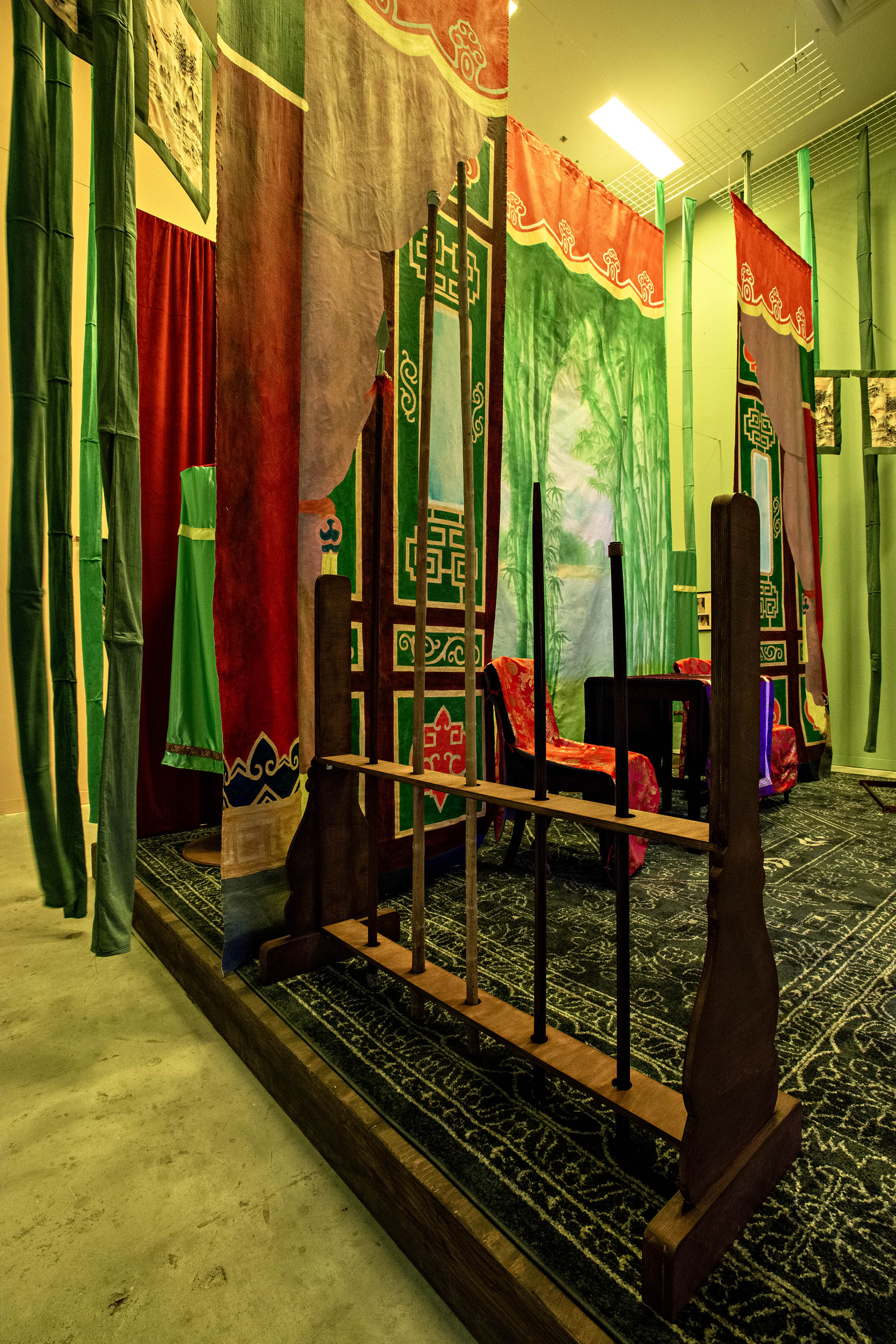 Vue latérale de l’installation Parfum des foudres depuis le côté gauche de la scène, dévoilant des couches de tissus colorés, des banderoles suspendues et des accessoires de théâtre.