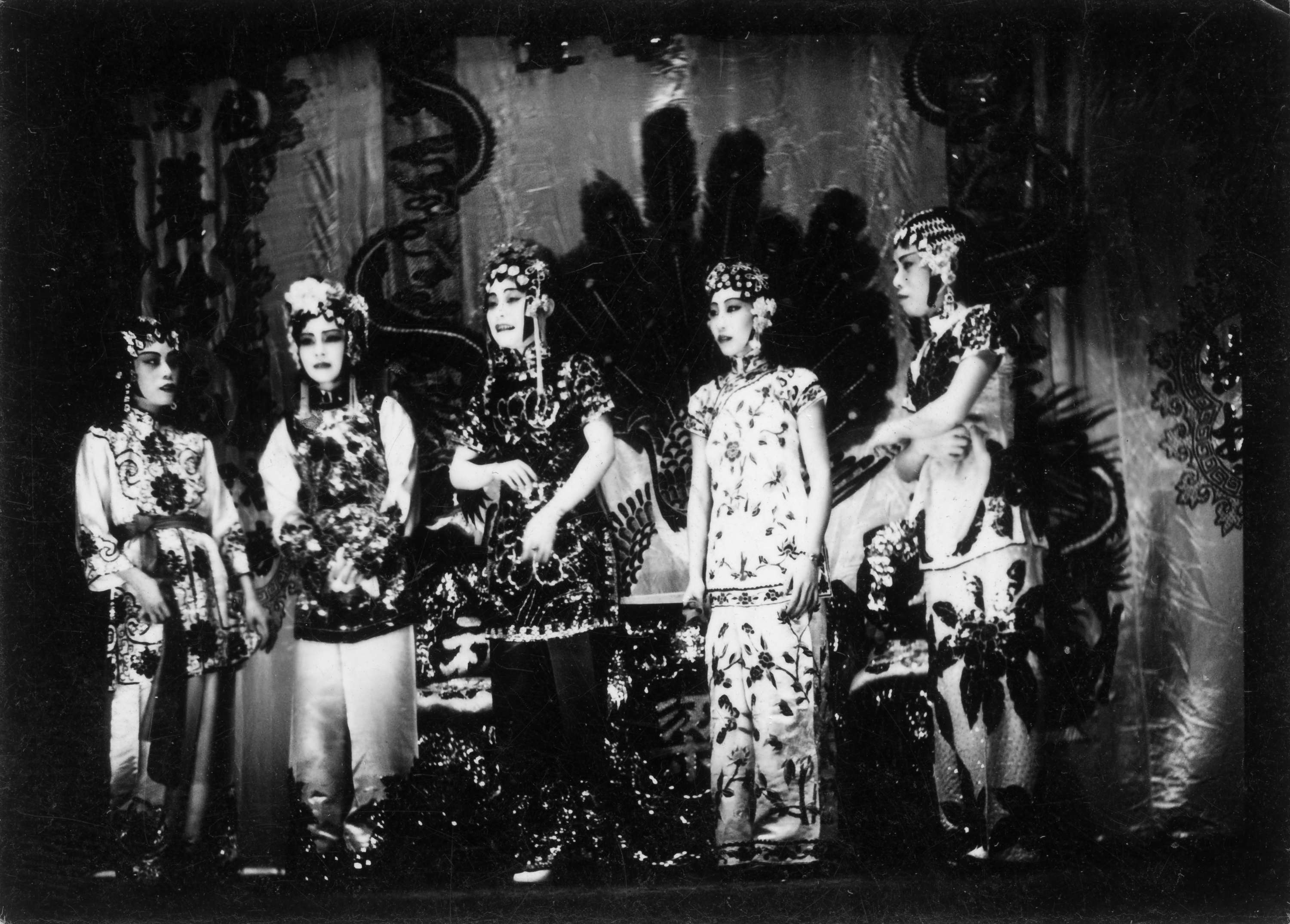 <span style="font-weight: 400;">Photo en noir et blanc de cinq artistes d’opéra chinois debout en rang sur scène, face au public, vêtues de costumes traditionnels richement brodés.</span>