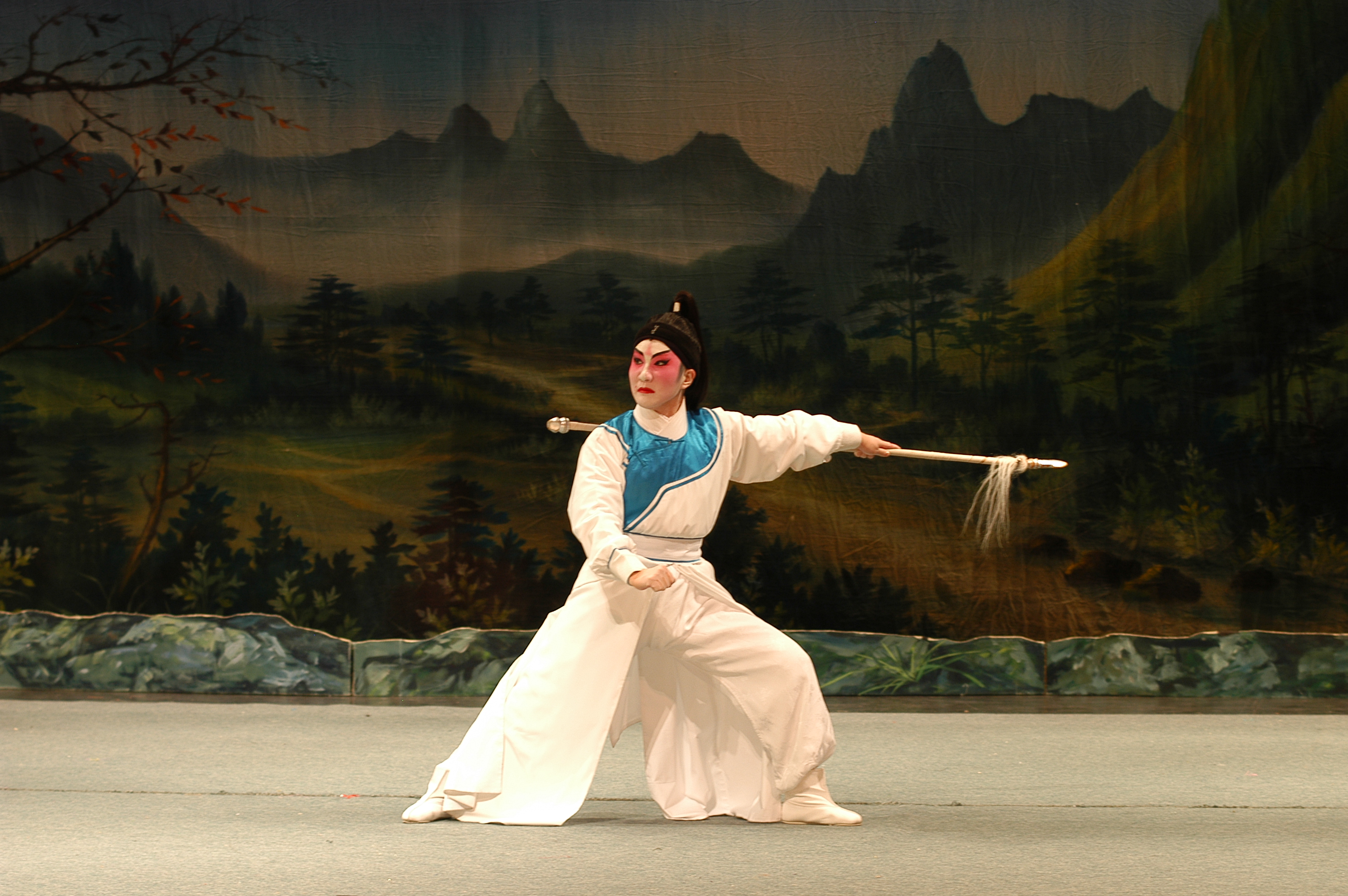 <span style="font-weight: 400;">A lower-ranking warrior in a simple blue-and-white battle costume holds a spear in a martial arts stance following a strike.</span>