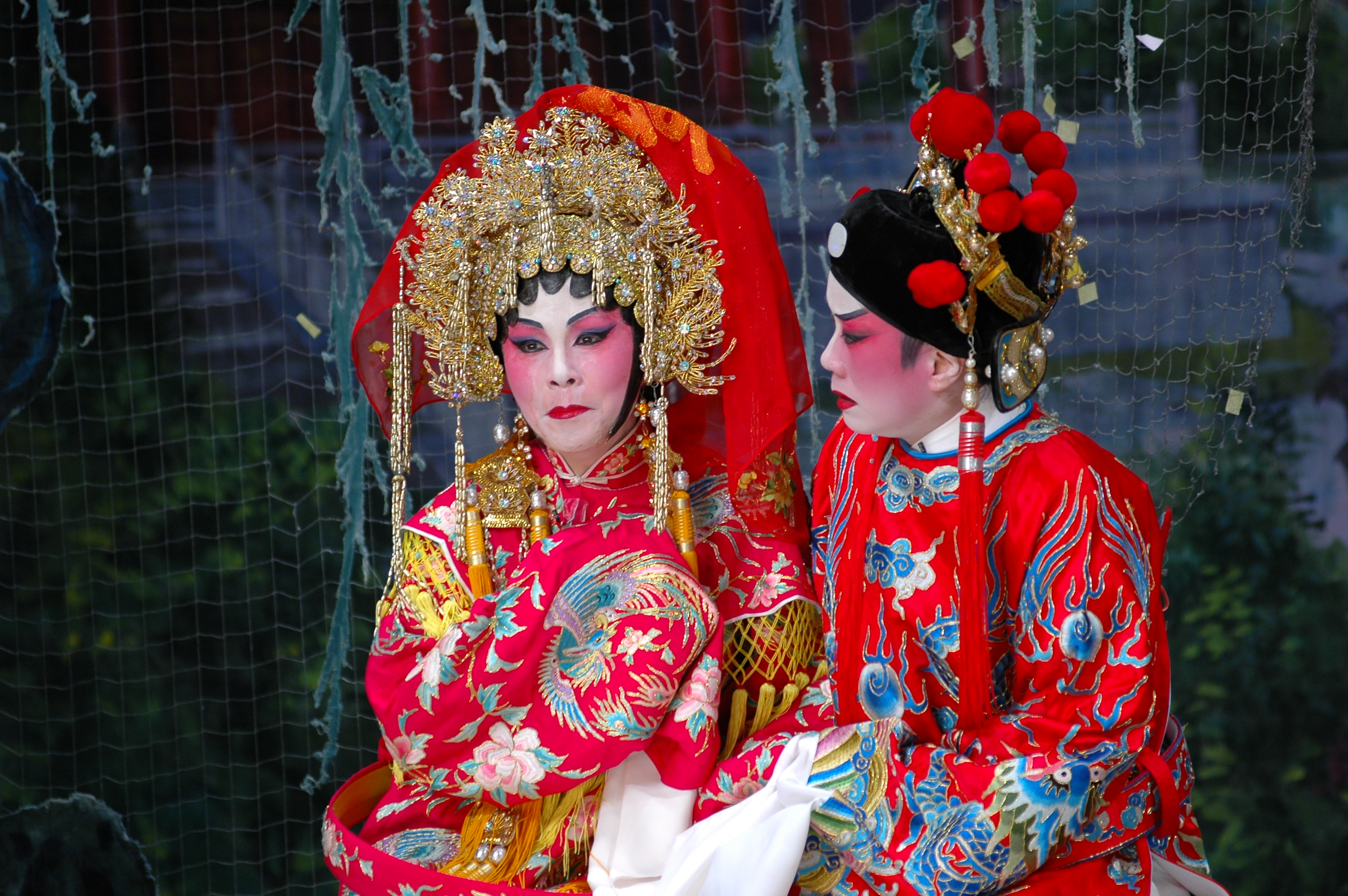 <span style="font-weight: 400;">La princesse Cheung Ping et le prince consort Zhou, vêtu·e·s de costumes traditionnels d’opéra cantonais, sont assis·e·s côte à côte sur un banc à l’extérieur, s’enlaçant avec le regard sombre.</span>
