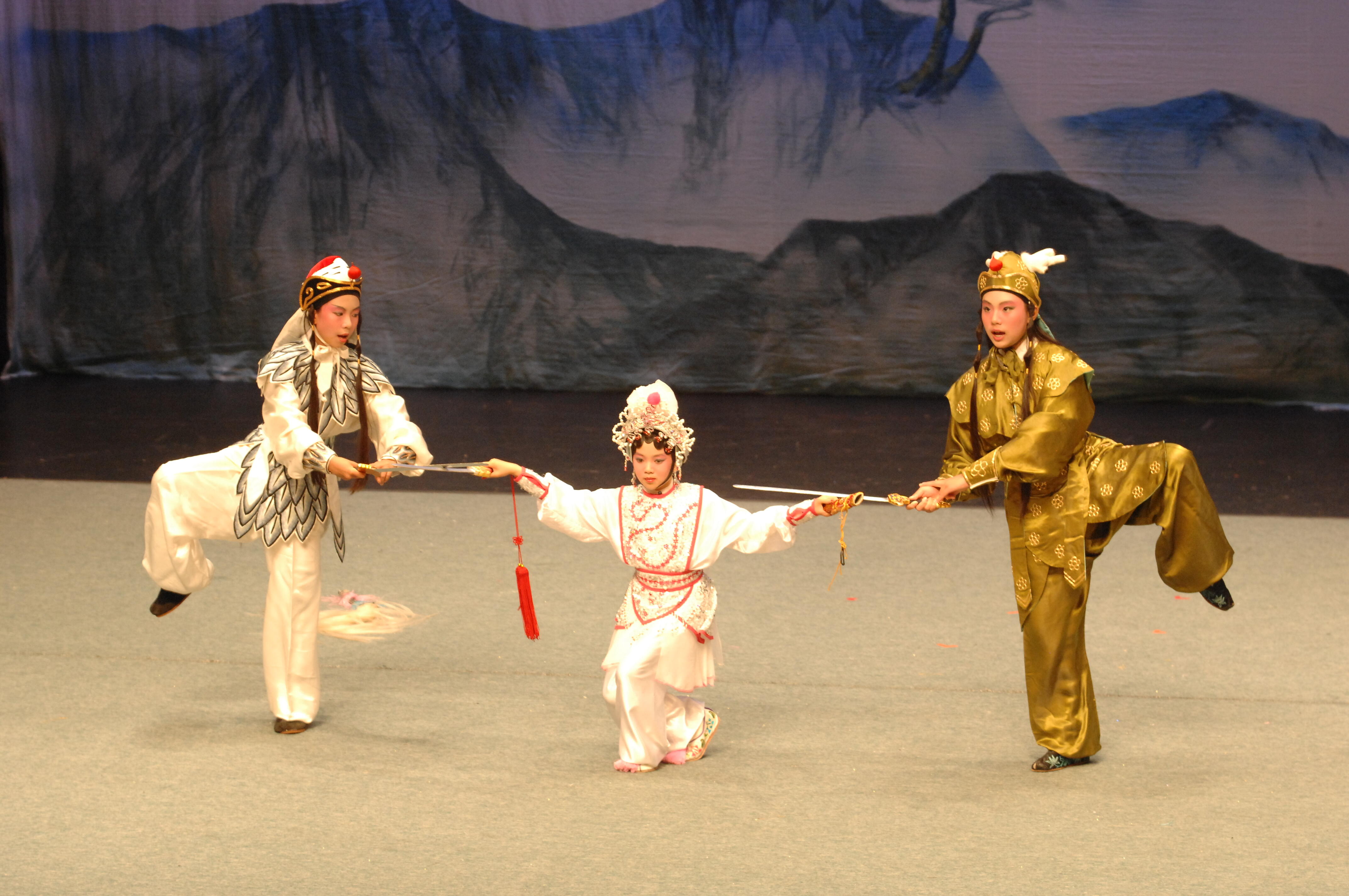 <span style="font-weight: 400;">Trois jeunes portant des costumes élaborés exécutent des mouvements énergiques sur scène, devant une toile de fond sur laquelle est peinte une montagne.</span>