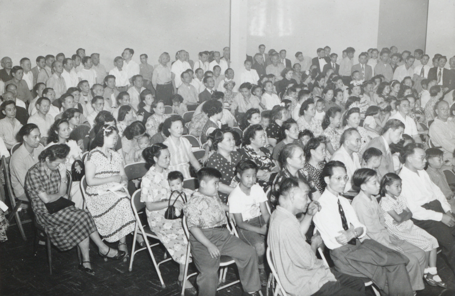 <span style="font-weight: 400;">Des hommes, des femmes et des enfants ont pris place sur des chaises pliantes en métal. La salle est si pleine que deux ou trois rangées d’hommes se tiennent debout à l’arrière.</span>