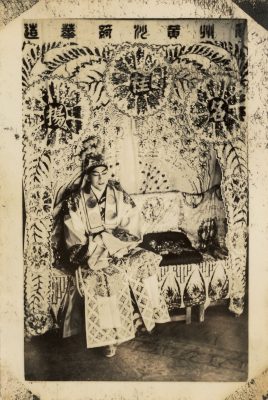 <span style="font-weight: 400;">A performer in an elaborate costume and headdress sits on a chair that resembles a prop throne, giving a regal appearance.</span>