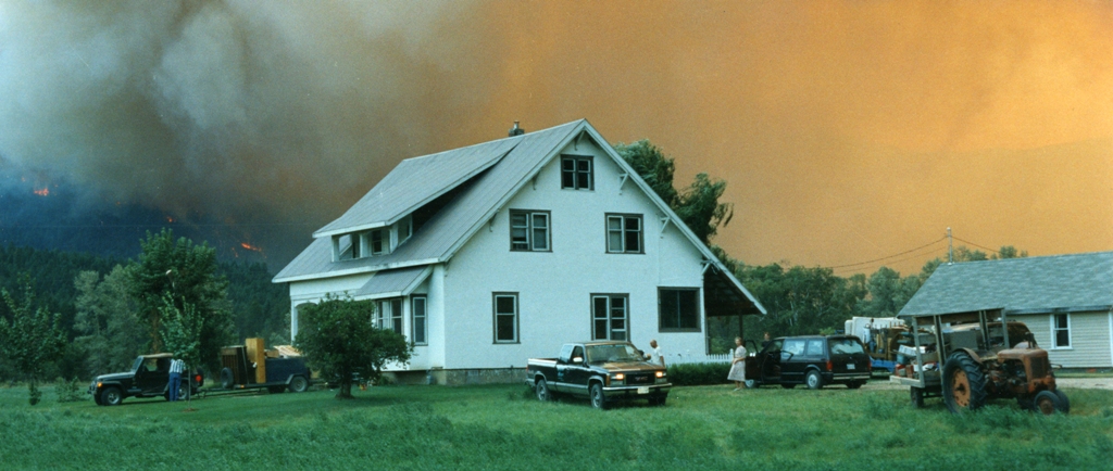 A family evacuates from their home. Fire rages in the background - Une famille fuit leur maison. Un feu fait rage à l'arrière plan